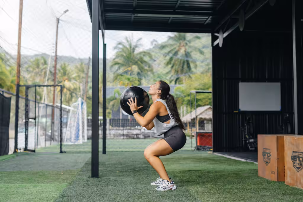 Female athlete performing wall ball squats during a complete fitness session at an outdoor gym in Koh Samui